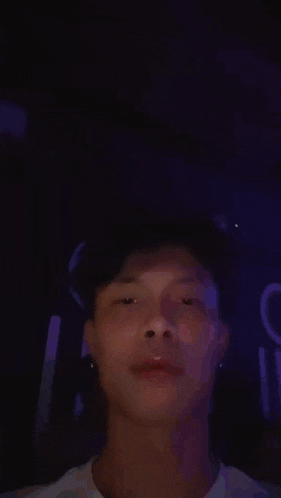 a young man is making a funny face with his eyes closed while sitting in a dark room .