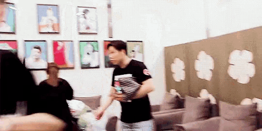 a man in a black shirt is standing in a room with pictures on the wall
