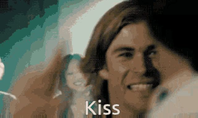 a man and a woman are kissing in a blurry photo with the word kiss in the corner .