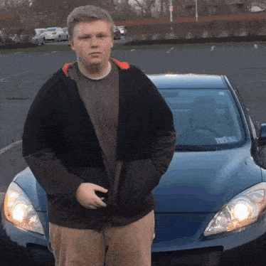 a young man stands in front of a blue car with a license plate that says ' tc ' on it