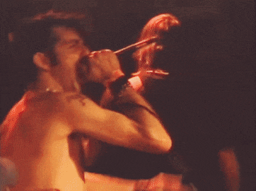 a shirtless man singing into a microphone with a tattoo on his shoulder that says ' jesus '