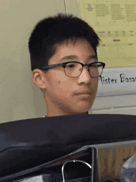 a boy wearing glasses sits in front of a sign that says mister basal