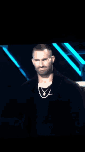 a man with a beard is wearing a black jacket and necklace