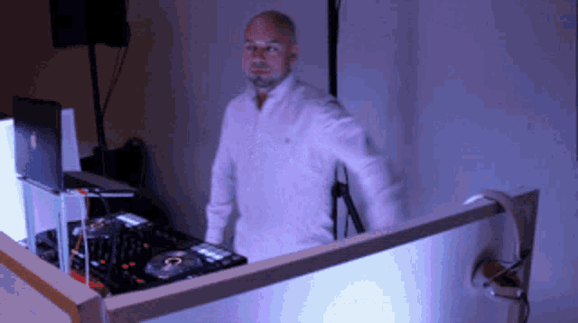 a man in a white shirt stands in front of a dj set