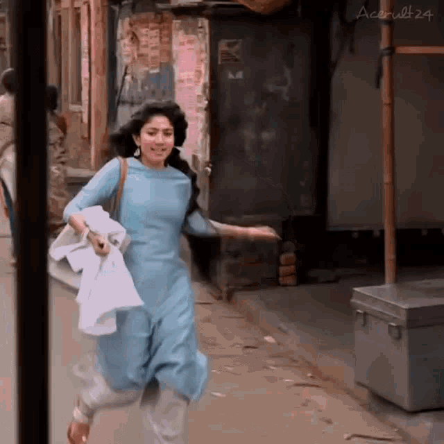 a woman in a blue dress is running down a street holding a white shirt .