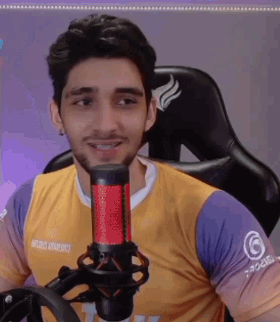 a man in a yellow and purple shirt is sitting in front of a microphone and smiling