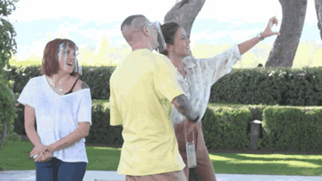 a man wearing a yellow shirt is standing next to two women