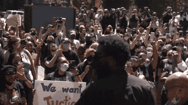 a man stands in front of a crowd holding a sign that reads we want justice