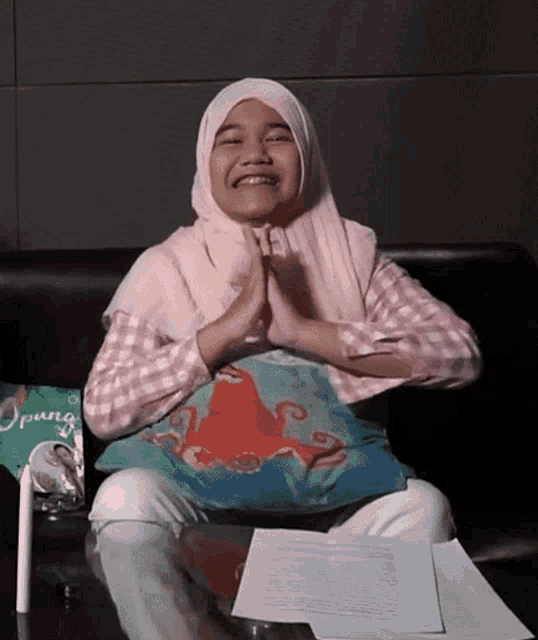 a girl wearing a hijab is sitting on a couch with an octopus pillow and a package of opung behind her