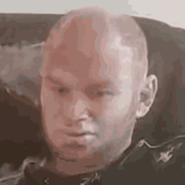 a bald man with a beard is sitting on a couch and making a funny face .