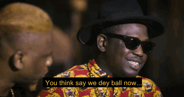 a man in a hat and sunglasses says you think say we dey ball now