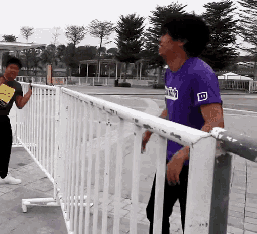 a man in a purple shirt that says twitch is standing next to a white railing