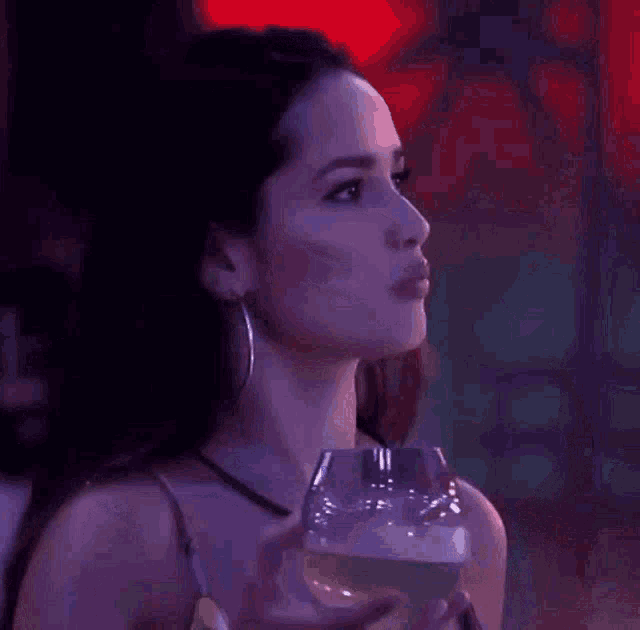 a woman is holding a glass of wine in her hand and looking at the camera .
