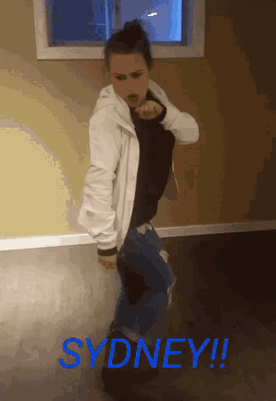 a woman in a white jacket is dancing in a room with the word sydney in blue
