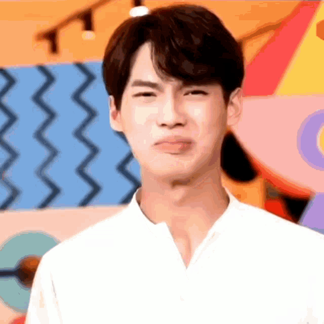 a young man is making a funny face while standing in front of a colorful background .