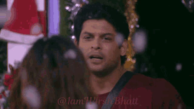 a man in a red shirt is talking to a woman in front of a christmas tree