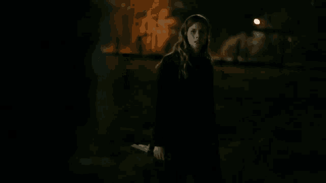 a woman in a black coat is holding a knife in the dark