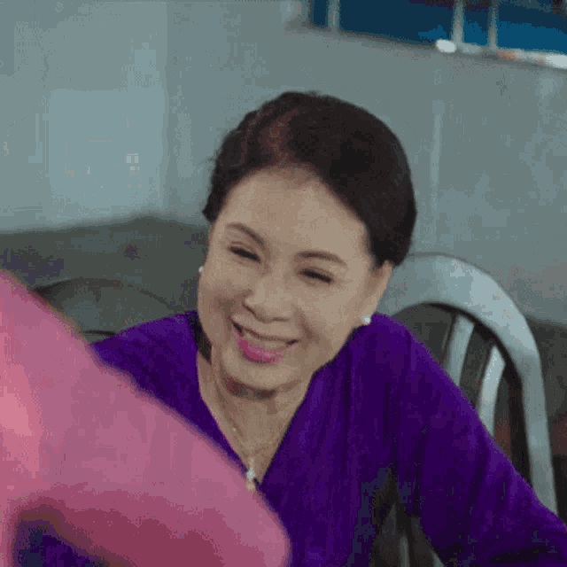 a woman in a purple shirt is smiling and sitting in a chair