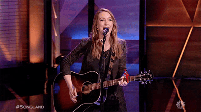 a woman singing into a microphone while holding a guitar in front of her