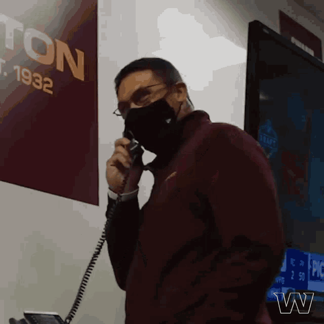 a man wearing a mask is talking on a phone in front of a sign that says " est 1932 "