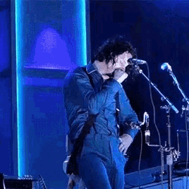 a man in a blue jumpsuit is singing into a microphone while playing a guitar .