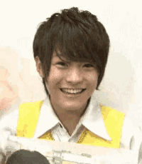 a young man wearing a yellow vest and a white shirt is smiling and holding a sign .