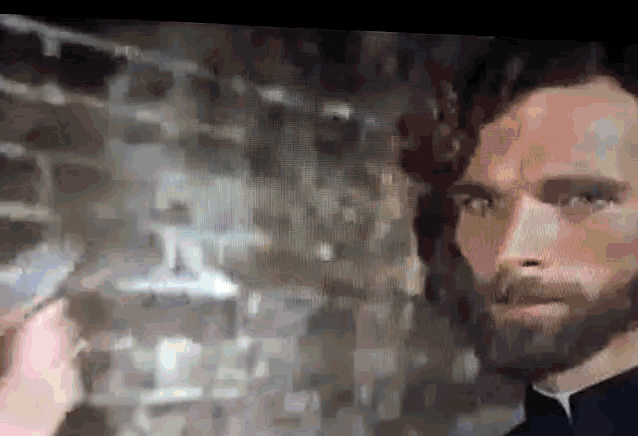 a man with a beard is standing in front of a brick wall in a dark room .
