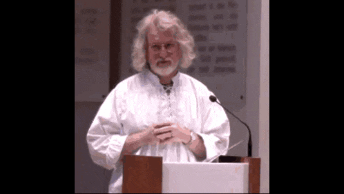a man in a white shirt stands at a podium with a microphone