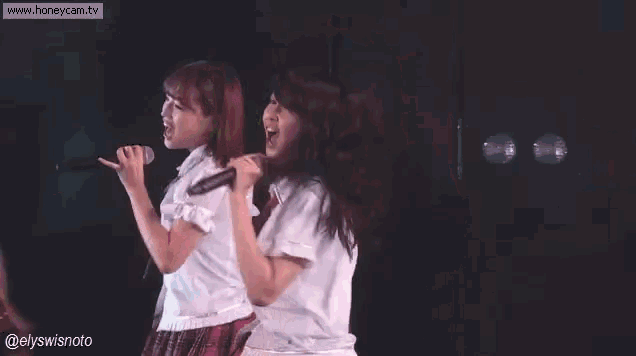 two girls are singing into microphones on a stage while standing next to each other .