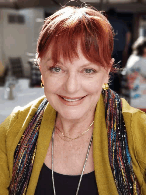 a woman with red hair and a scarf around her neck smiles
