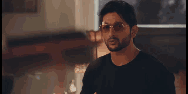 a man wearing sunglasses and a black shirt is standing in a room .