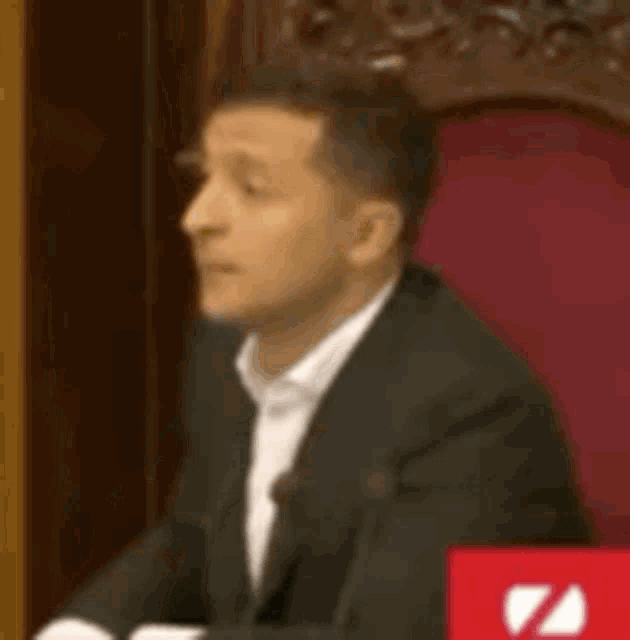 a man in a suit is sitting in a red chair holding a microphone and making a funny face .