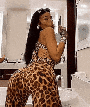 a woman in a leopard print jumpsuit is taking a picture of herself in the bathroom .