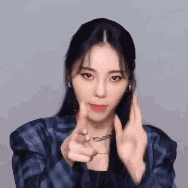 a woman in a plaid jacket is pointing at the camera with her hands .