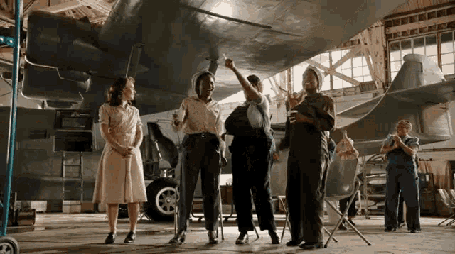 a group of women standing in front of a plane in a hangar
