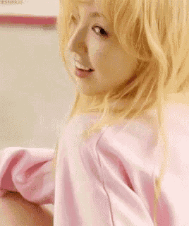 a close up of a woman with blonde hair wearing a pink shirt and smiling .