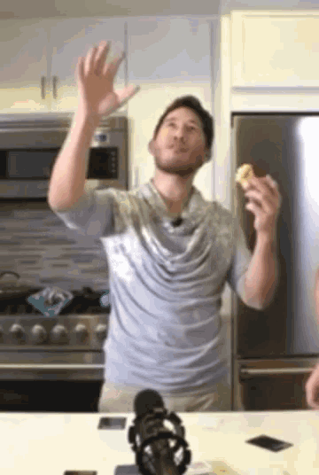 a man in a grey shirt is standing in a kitchen holding a banana