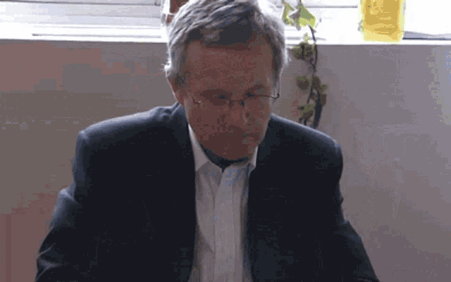 a man wearing glasses and a suit looks down at something