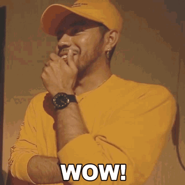 a man wearing a yellow shirt and a yellow hat is covering his mouth with his hand and says wow