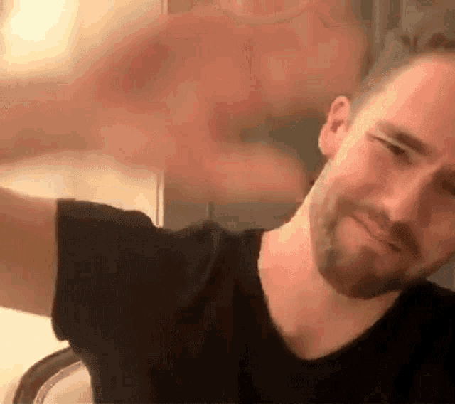a man with a beard is wearing a black shirt and making a face .