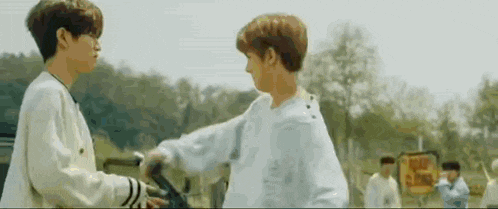 two young men are standing next to each other in a field and hugging each other .