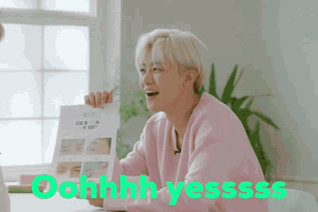 a man in a pink sweater is smiling and holding a piece of paper that says ohhhh yessss