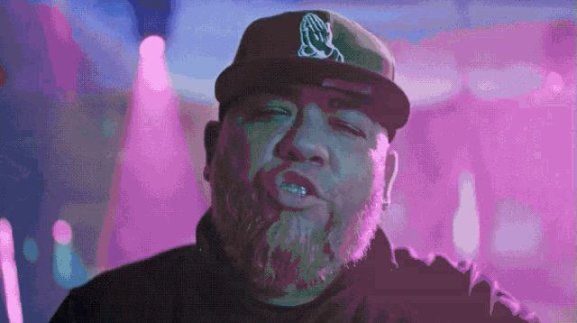 a man with a beard is wearing a hat with a praying hands logo on it