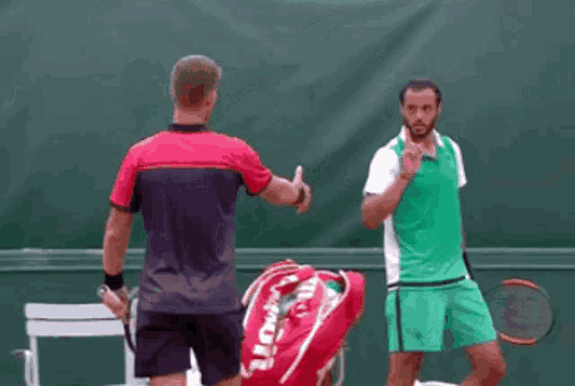 two tennis players shake hands on a court with a wilson bag behind them