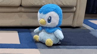 a blue and white stuffed penguin is sitting on a blue and white rug in front of a couch .