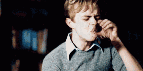 a man in a sweater is drinking from a glass while sitting in a dark room .