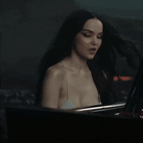 a woman with long black hair is singing into a microphone while sitting in front of a piano