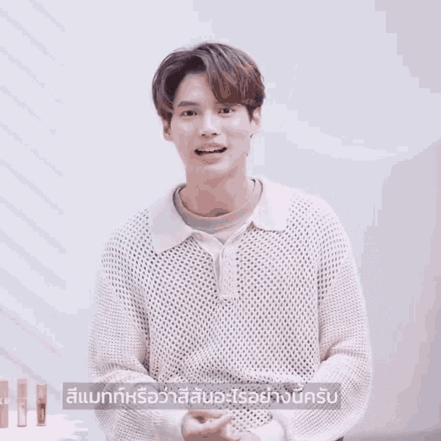 a young man wearing a white sweater and a brown shirt is talking in a video .