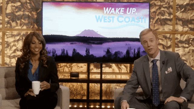 a man and a woman are sitting in front of a screen that says wake up west coast