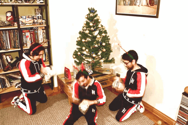 a group of men are kneeling in front of a christmas tree and one of them has the letter h on his shirt